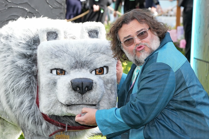 Jack Black with a grey beard and brown hair in a blue suit posing with a Minecraft wolf